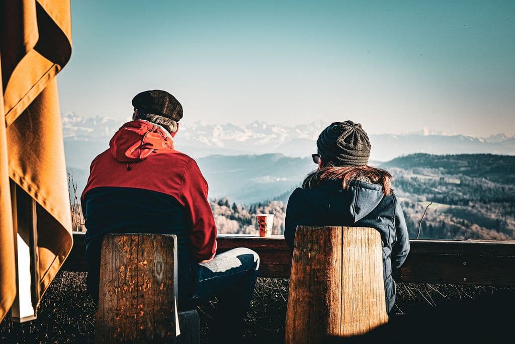 Una pareja sentada en una montaña mirando el paisaje.